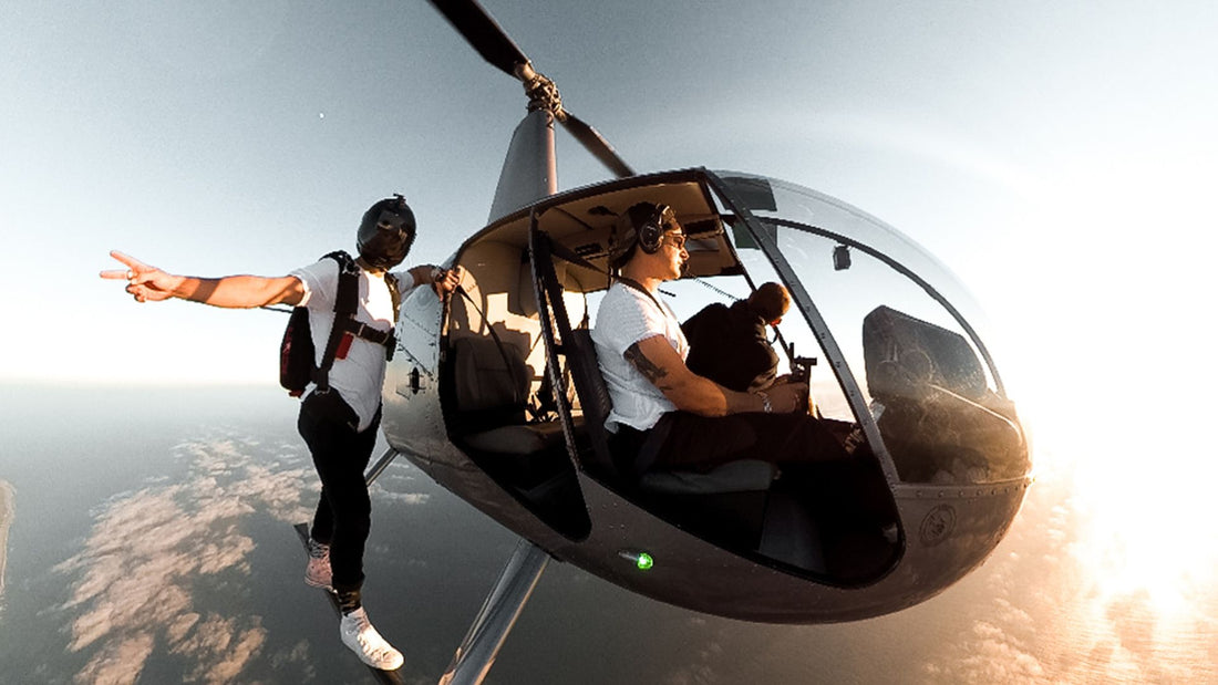 Skydiver balanced on outside of helicopter mid-flight over the earth with sun light
